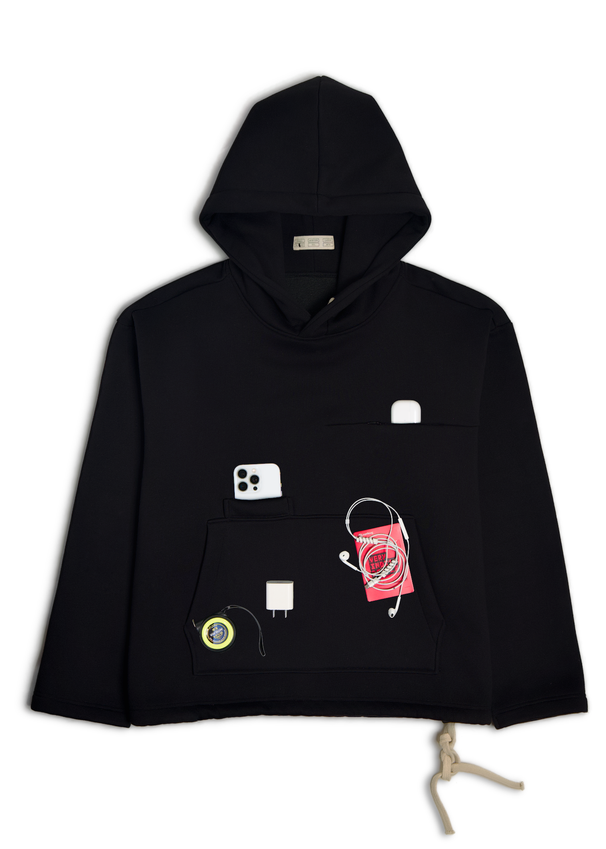 A black cropped hoodie with a kangaroo pocket decorated with various small accessories, including a red patterned pouch, a white USB-C cable, a white rectangular accessory, and a small circular patch, laid flat on a light gray background.